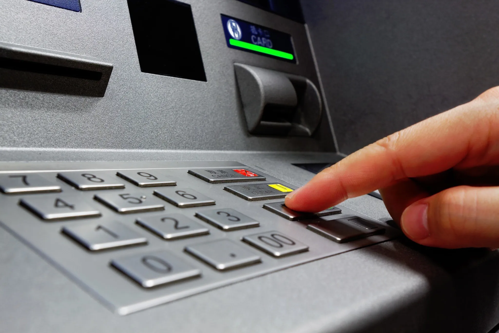 Person entering PIN on ATM keypad while withdrawing cash