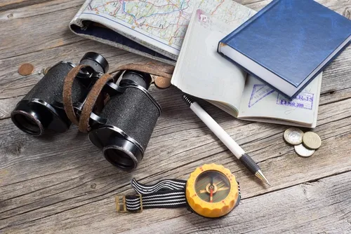 Safari booking essentials including a map, binoculars, travel journal, compass, and currency on a wooden table.